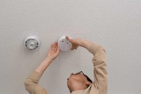 woman installing smoke detector on ceiling
